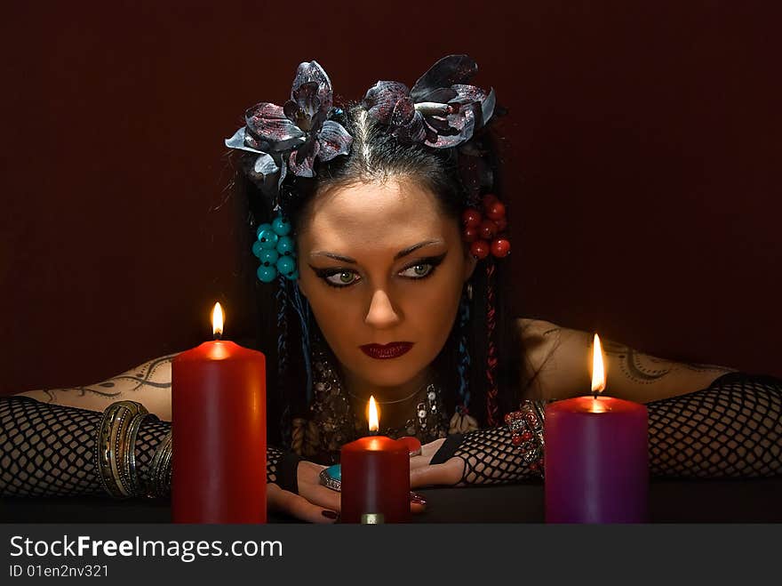 Young beautiful soothsayer with three candles on dark red background