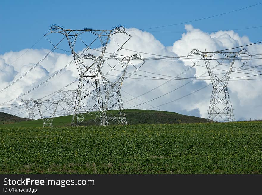 Electric poles on green farm fields with thunderstorm clouds in the background. Electric poles on green farm fields with thunderstorm clouds in the background