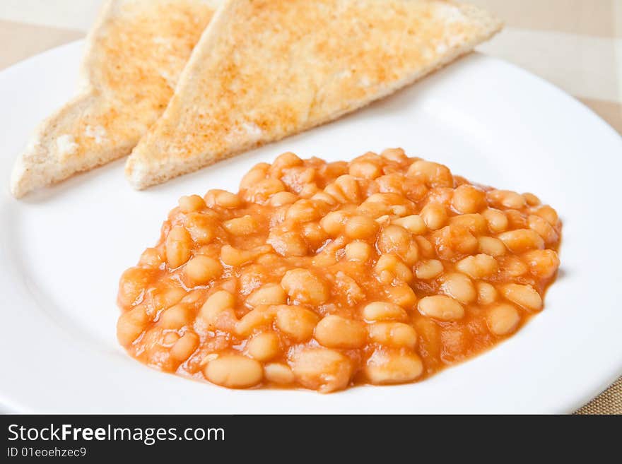 Baked beans on a white plate with fresh toast in the background. Baked beans on a white plate with fresh toast in the background