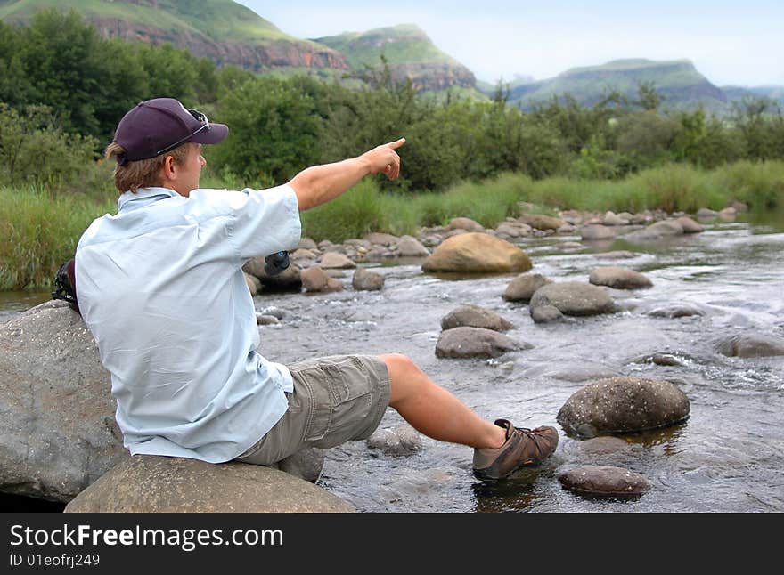 Male model sitting on rock in a mountain stream, pointing upstream. Male model sitting on rock in a mountain stream, pointing upstream