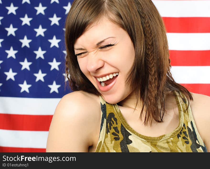 Happy laughing young woman standing opposite an American flag. Happy laughing young woman standing opposite an American flag