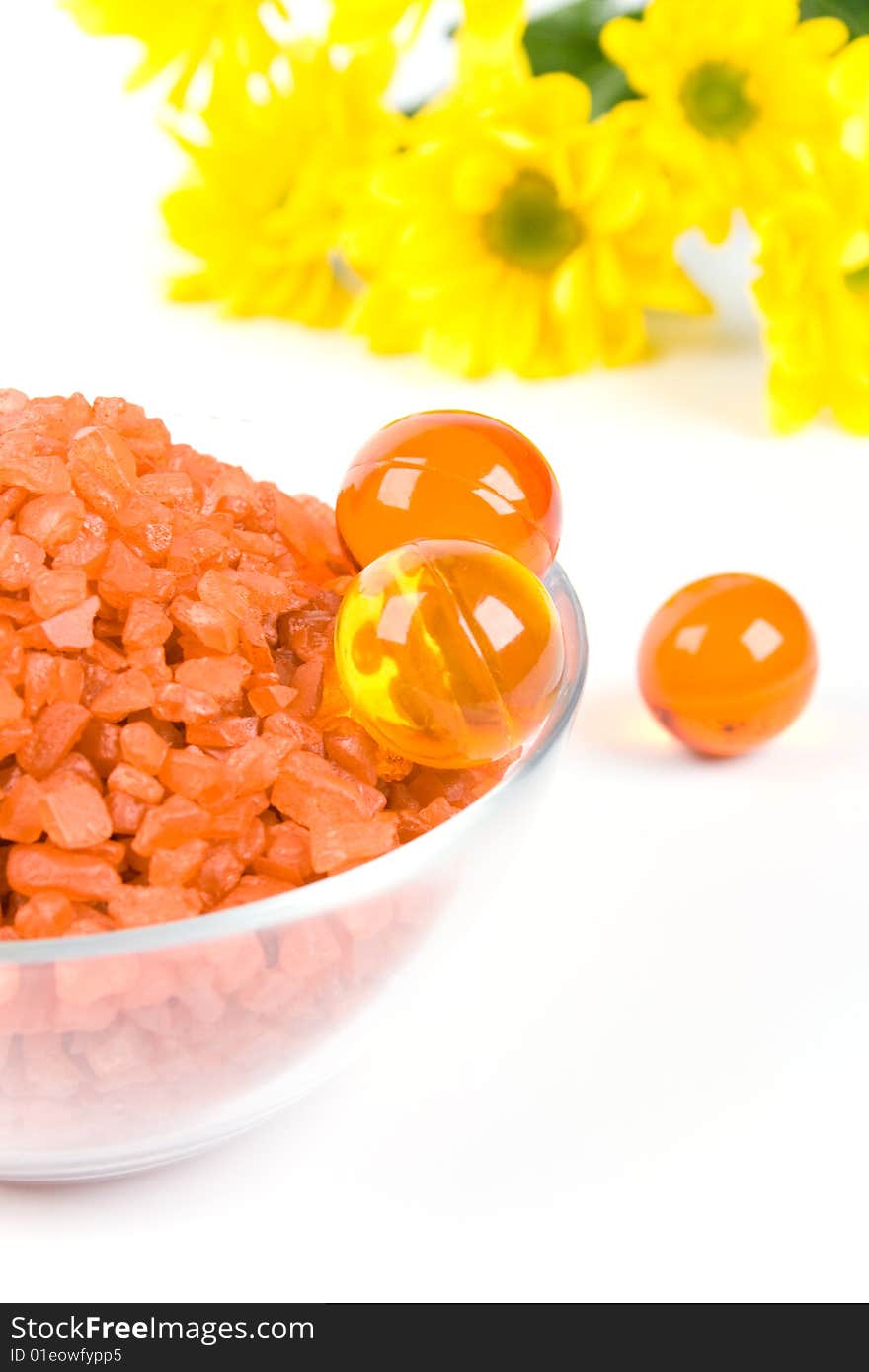 Spa pruducts: bath salt, oil balls in a bowl and yellow flowers