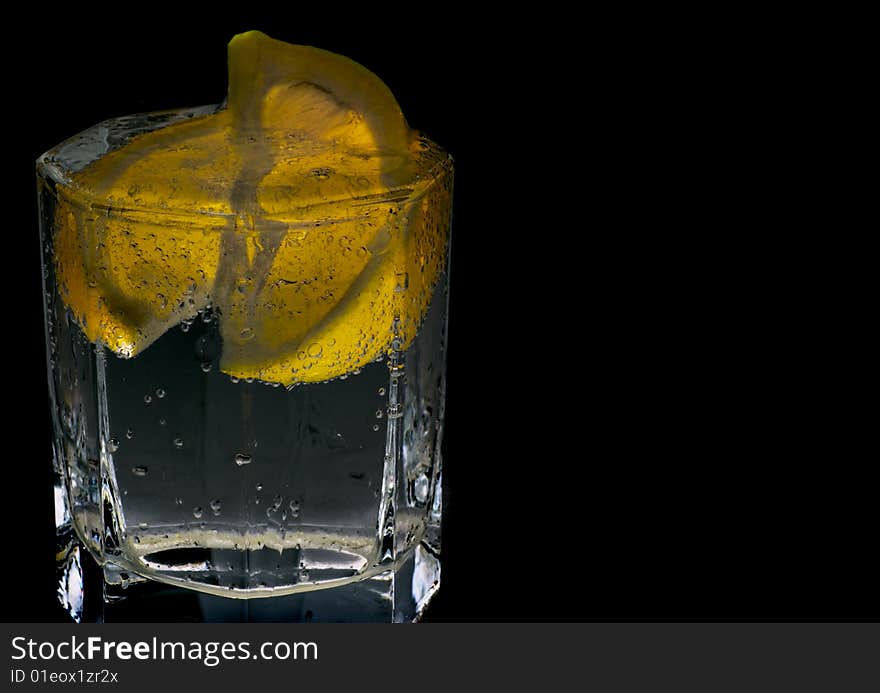 Glass with soda water and lemon slices on black background