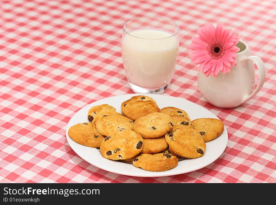 Plate of cookies with glass of milk and flower on checked tablecloth. Plate of cookies with glass of milk and flower on checked tablecloth.