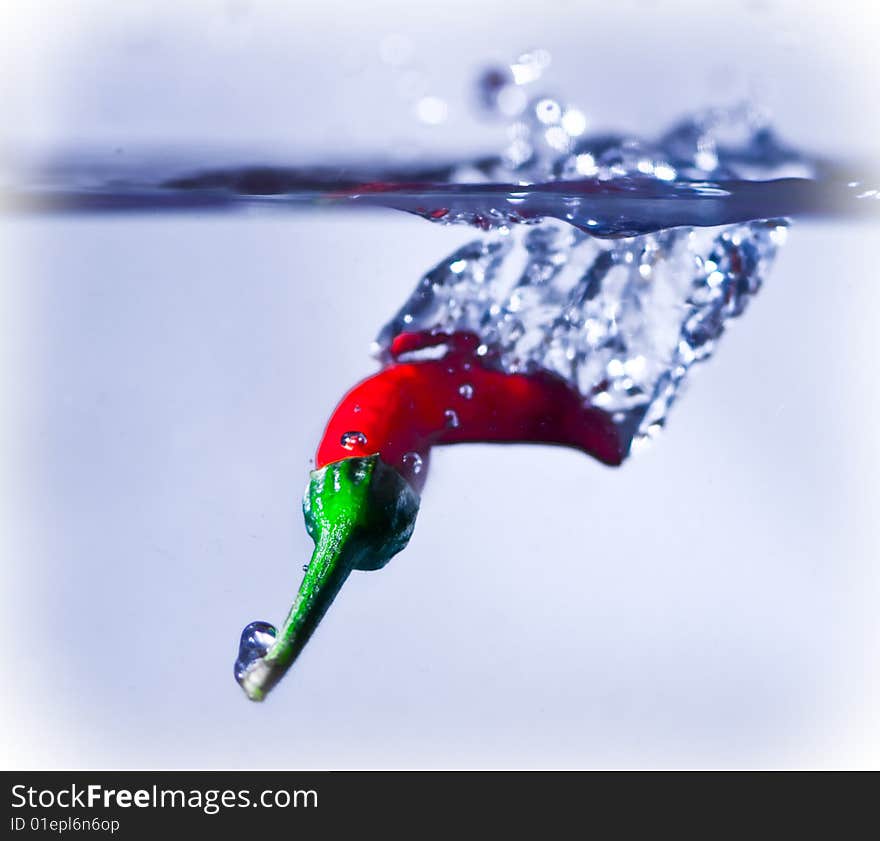 A red chilli splashing into water.