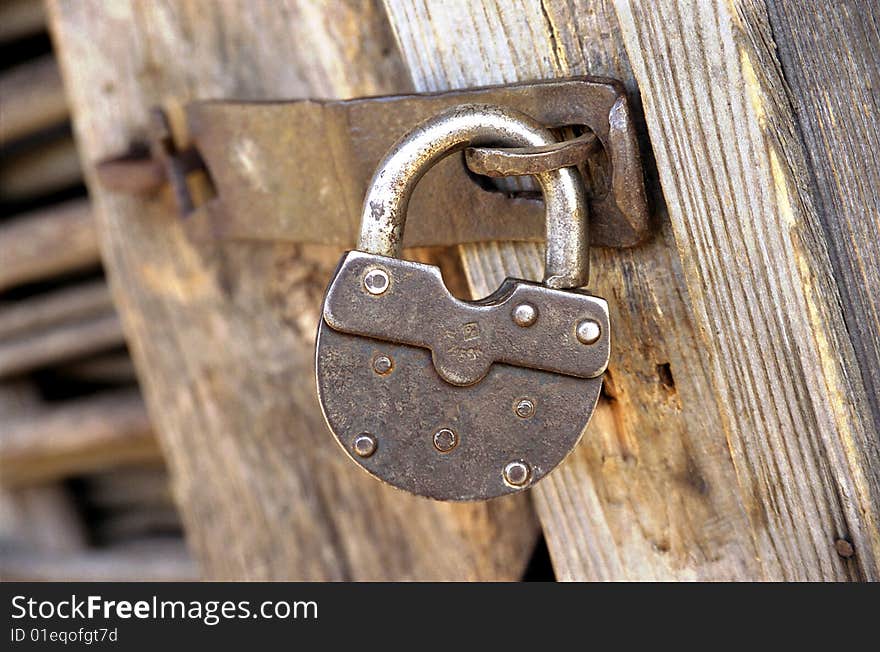 A metal lock is hanging on a wooden door. A metal lock is hanging on a wooden door