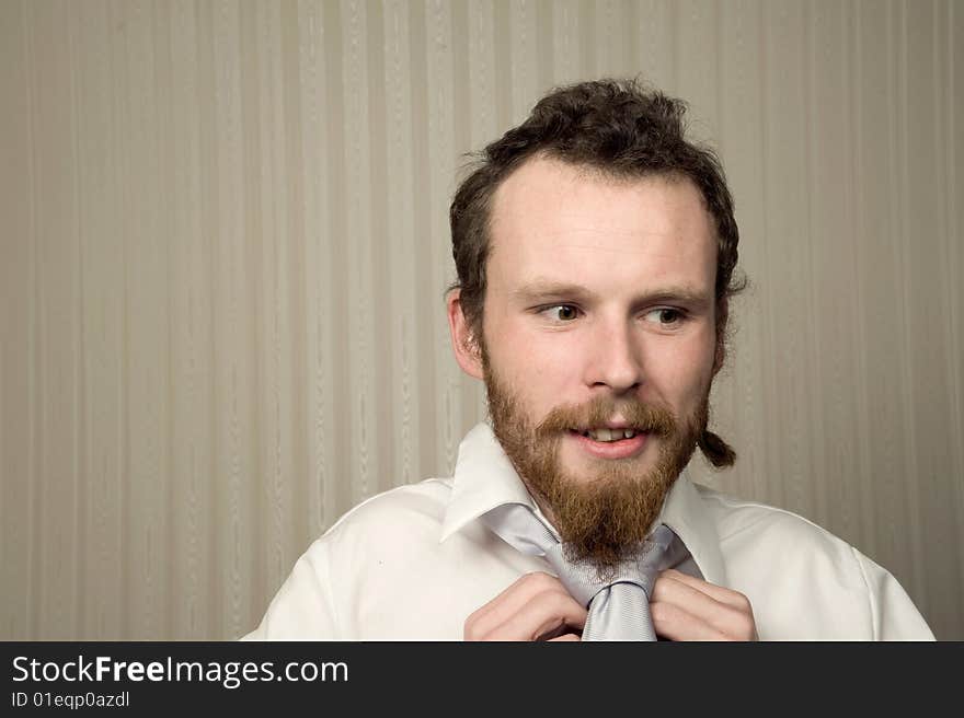 Young male with beard does up his tie with wallpaper behind. Young male with beard does up his tie with wallpaper behind