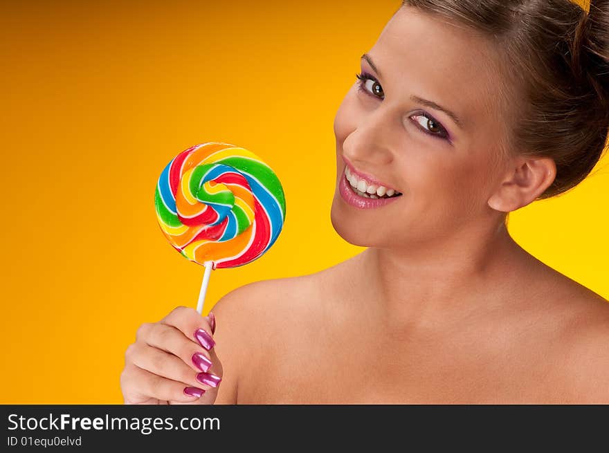 Smiling brunette woman with big lollipop on yellow background