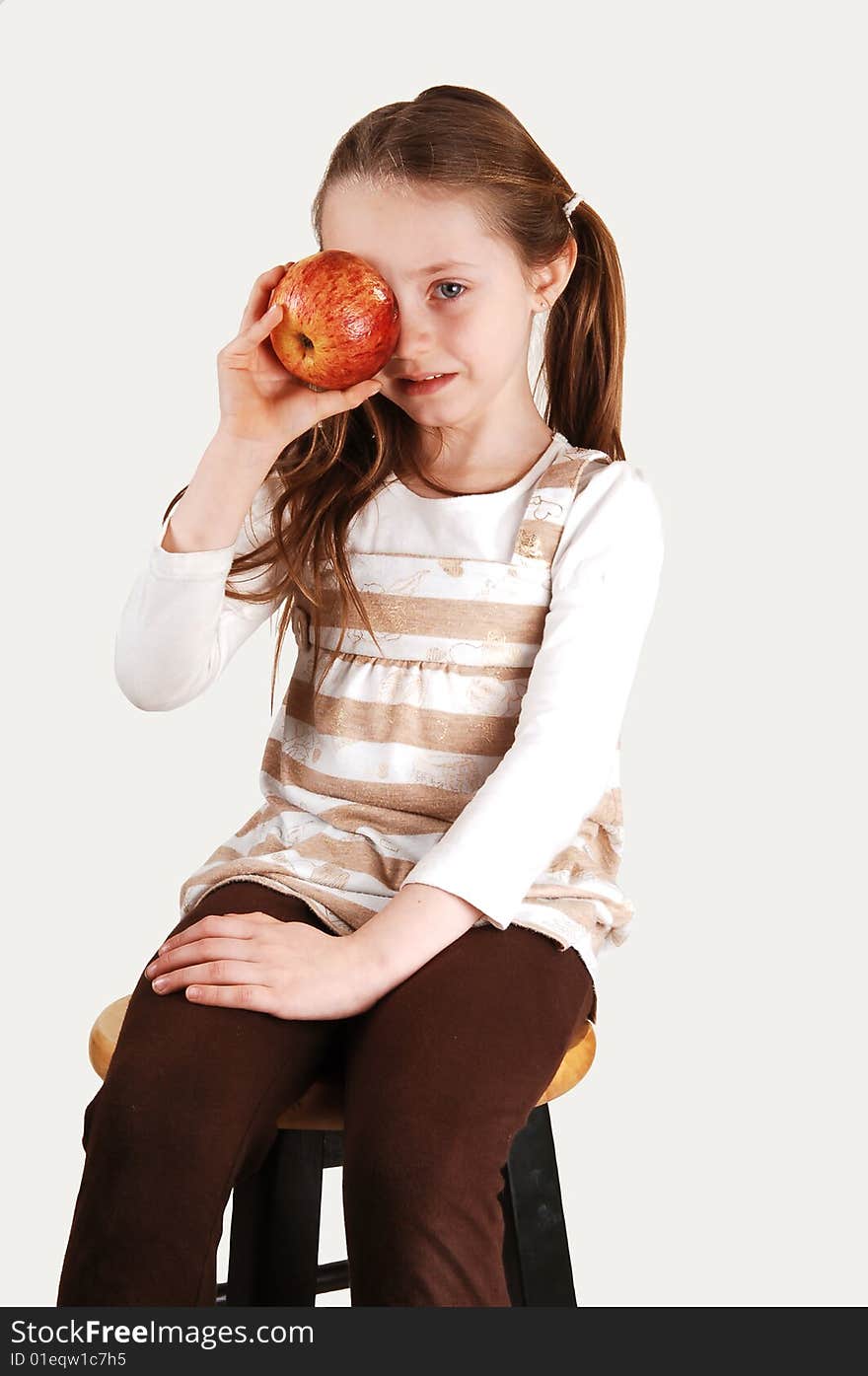 An little girl sitting on a high chair and holding a red apple on her right eye. An little girl sitting on a high chair and holding a red apple on her right eye.