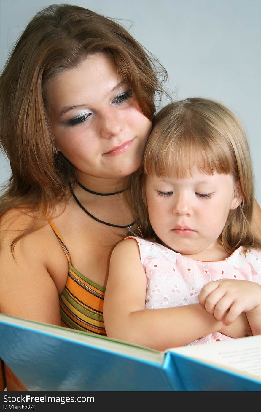 Two sisters different ages read the large book. Two sisters different ages read the large book