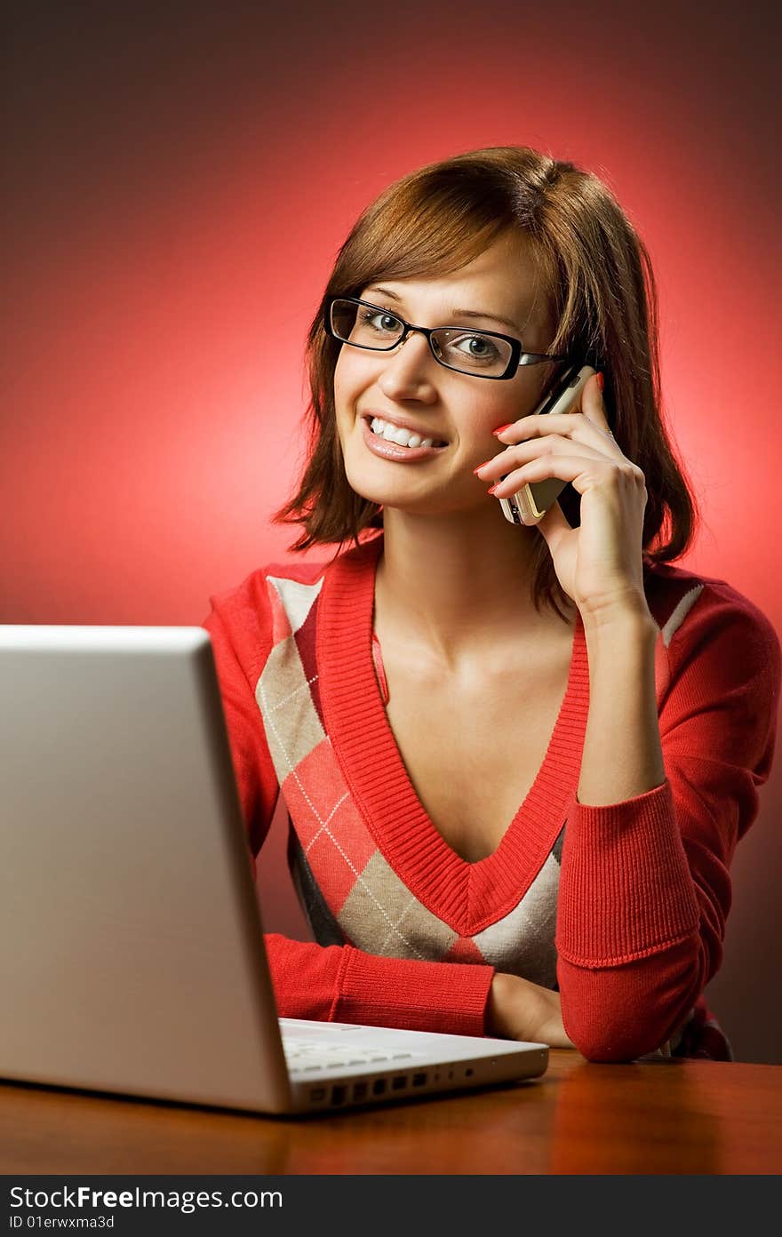 Beautiful smiling woman working on her laptop and talking on cell phone