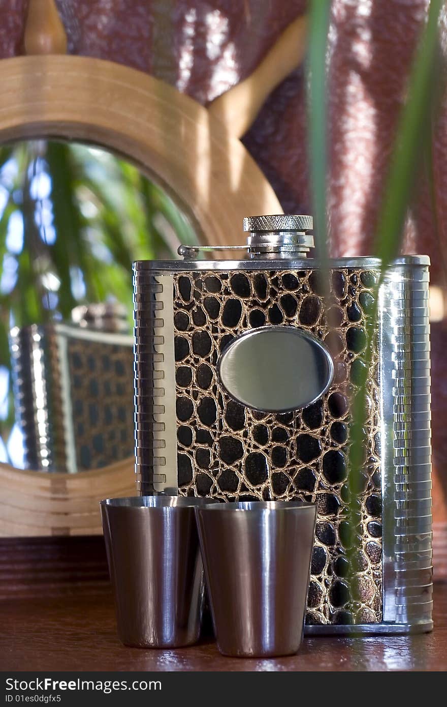 Elegantly decorated hipflask with two shots opposite the wheel-framed mirror