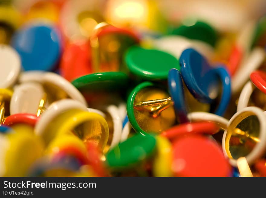 Coloured drawing pins scattered randomly with the middle one  in focus, red, blue green white & yellow pin covers with gold points. Coloured drawing pins scattered randomly with the middle one  in focus, red, blue green white & yellow pin covers with gold points