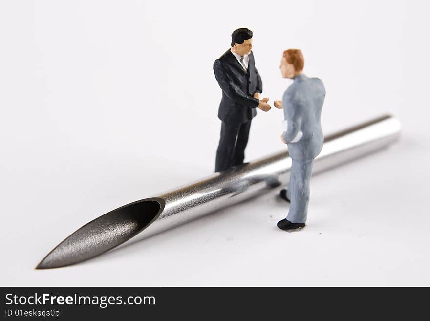 Miniature businessmen about to shake hands over a large bore needle. Miniature businessmen about to shake hands over a large bore needle.