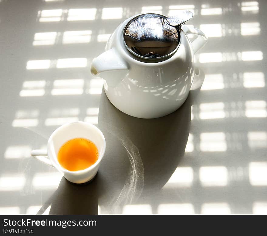 A picture of a cup of tea and a teapot basking under the sun. A picture of a cup of tea and a teapot basking under the sun