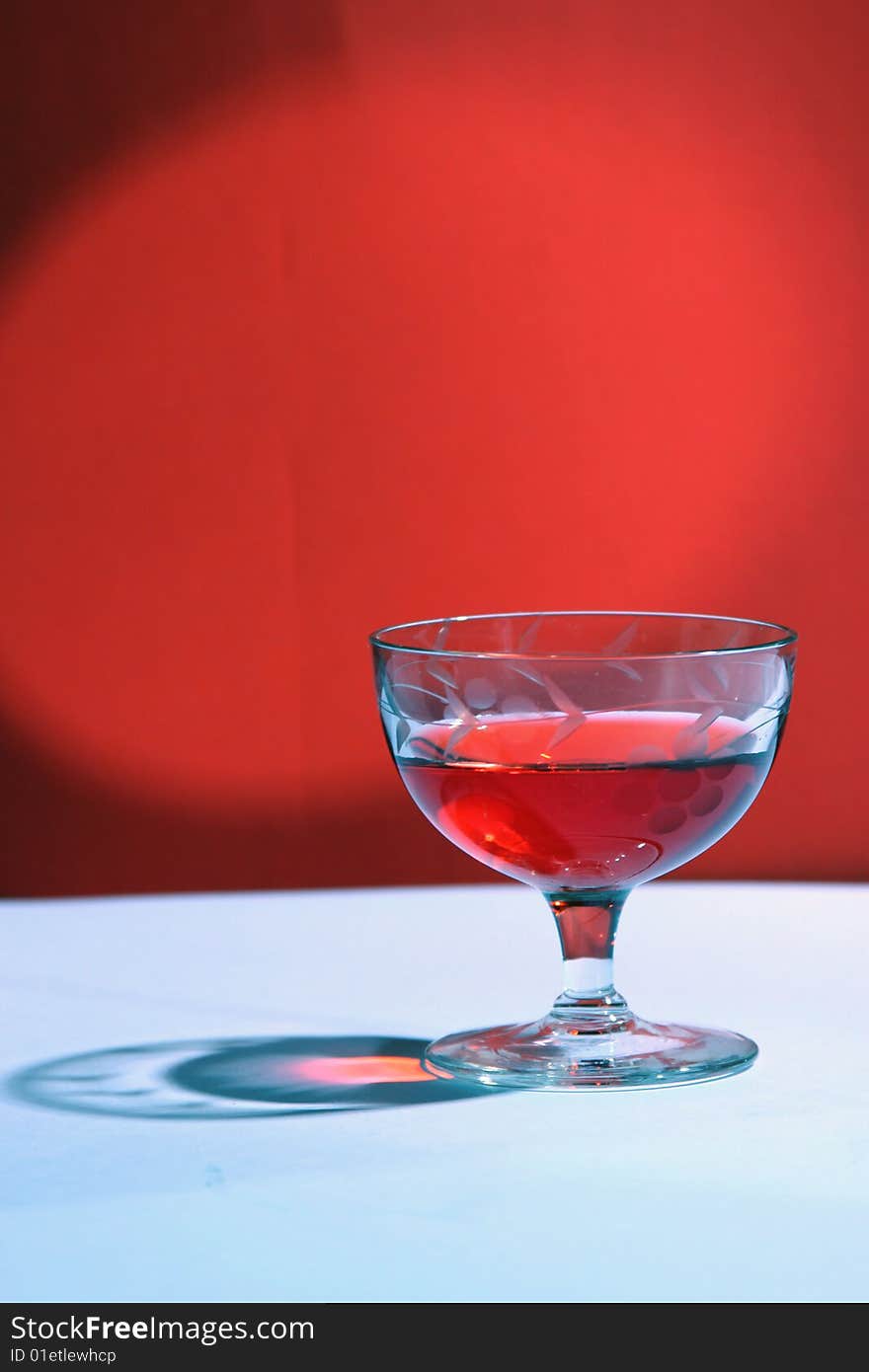 Photograph of a single glass of a red beverage on a red background.