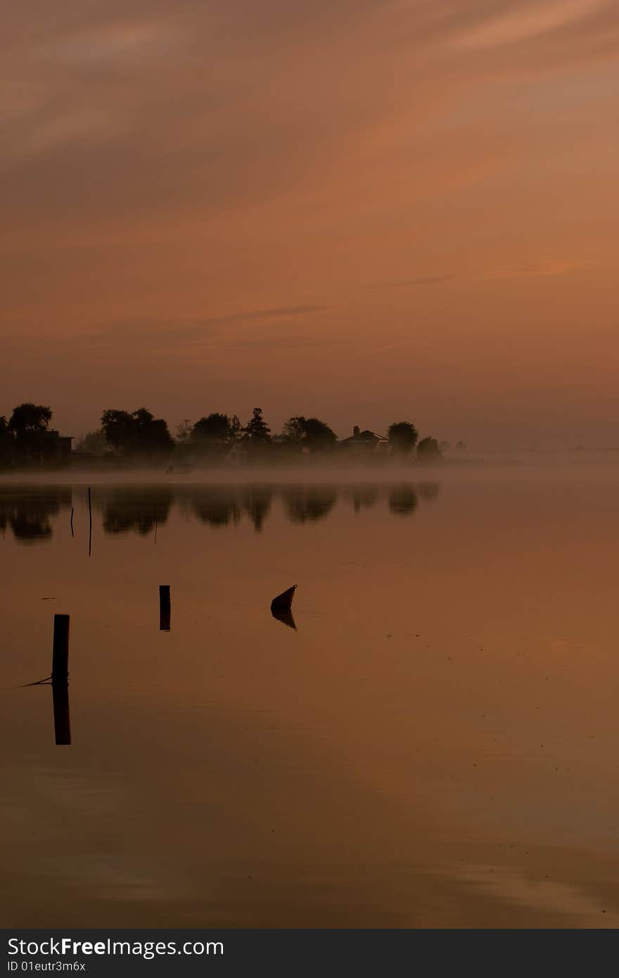 Dawn on a lake in northern holland. in the mist a fisherman is hauling in his nets. Dawn on a lake in northern holland. in the mist a fisherman is hauling in his nets.