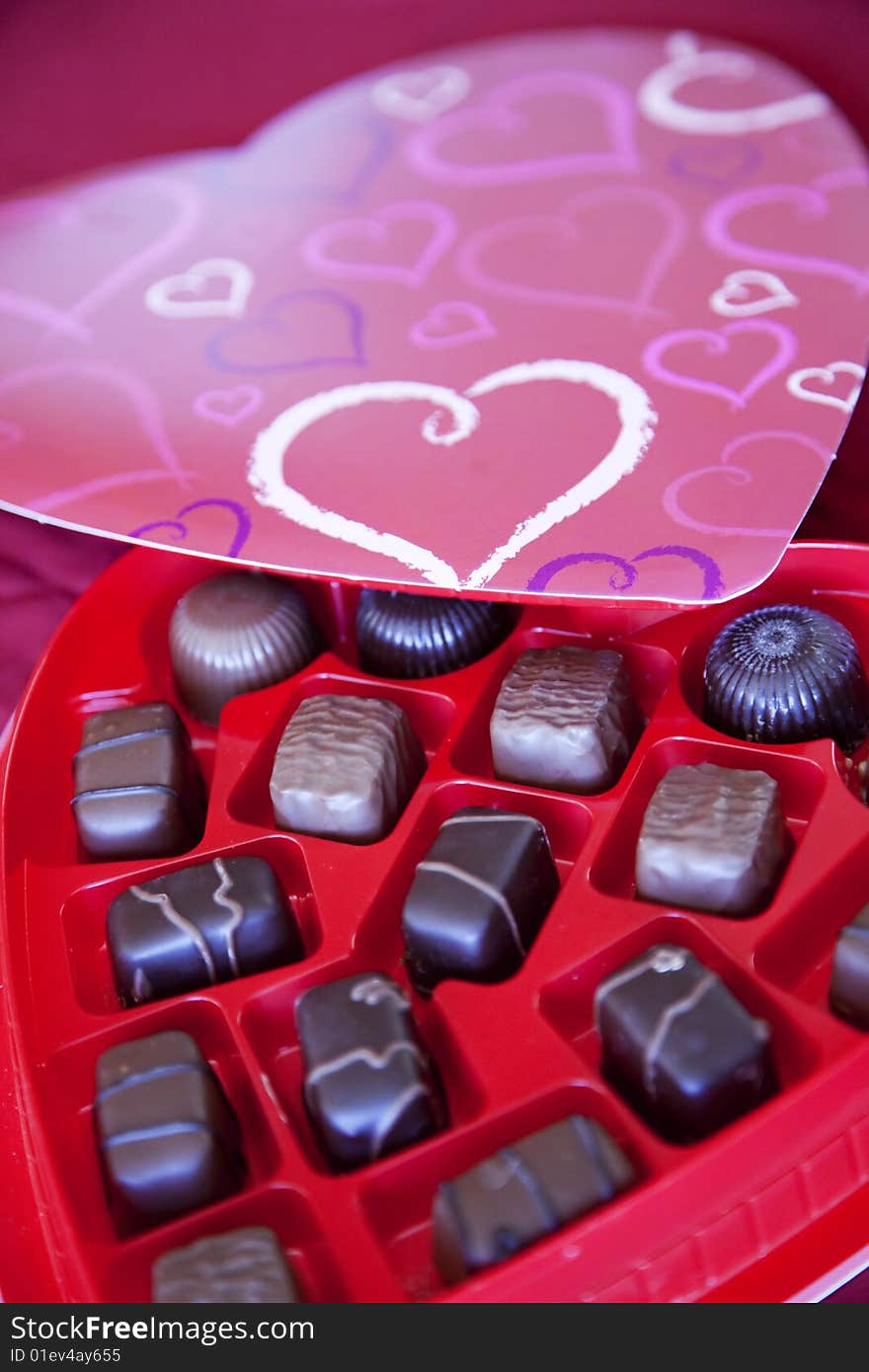 A box of chocolates is open with the top of the chocolate box on the outside rim of the pieces of chocolate. A box of chocolates is open with the top of the chocolate box on the outside rim of the pieces of chocolate