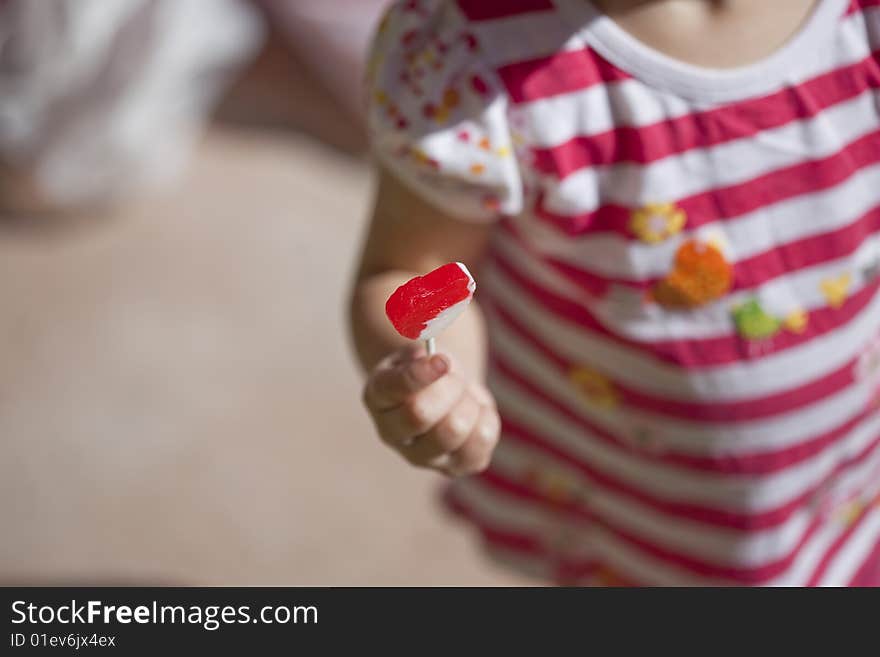 A little girl is holding up her little red sucker out to her side. A little girl is holding up her little red sucker out to her side