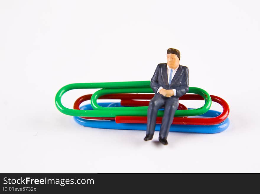 Miniature businessman sitting on paper clips. Miniature businessman sitting on paper clips