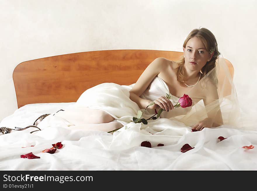 Bride lays on a bed with a red rose