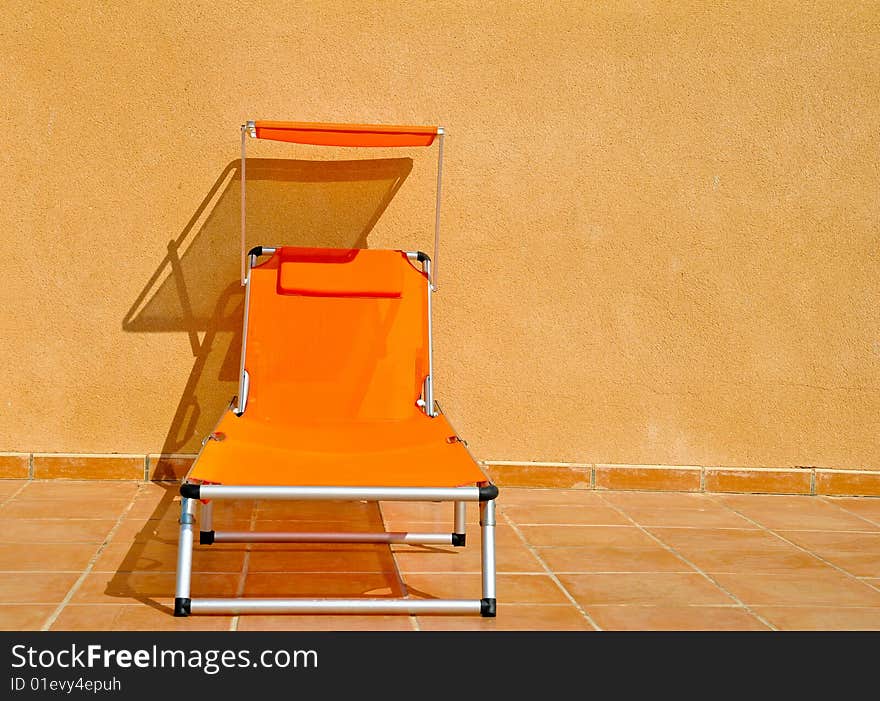 A vivid orange sun lounger on a tiled floor against a buff concrete wall