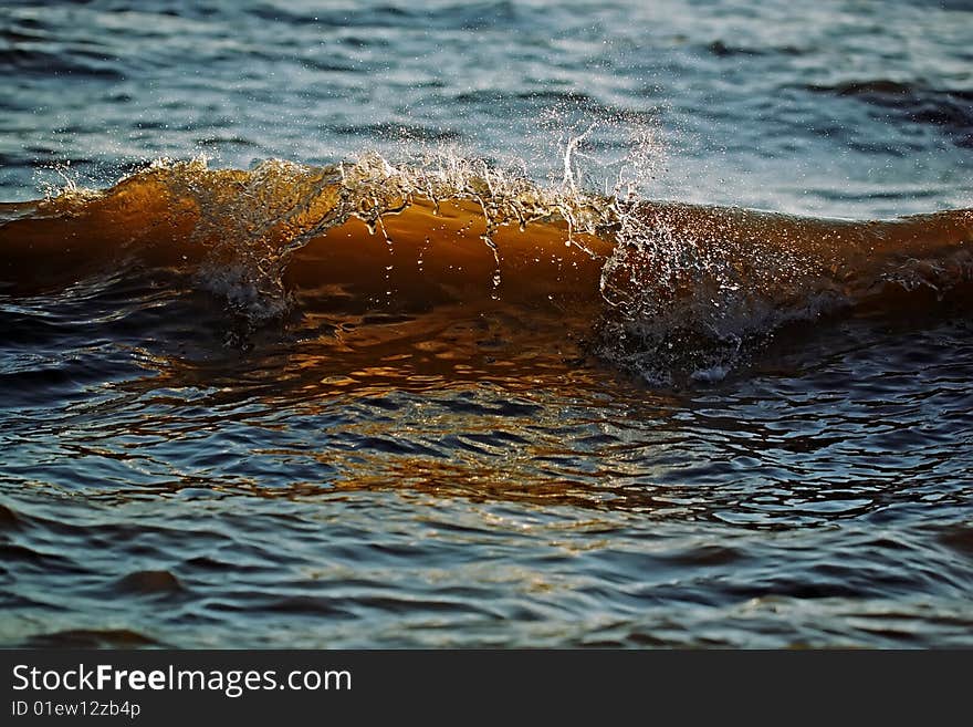 Amber wave with sparks of water broken from its crest covered by the sun on a decline. Amber wave with sparks of water broken from its crest covered by the sun on a decline.