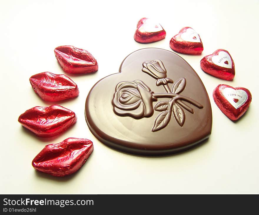 Heart and lips chocolates wrapped in red paper and a big heart chocolate with embossed flowers on it. Heart and lips chocolates wrapped in red paper and a big heart chocolate with embossed flowers on it