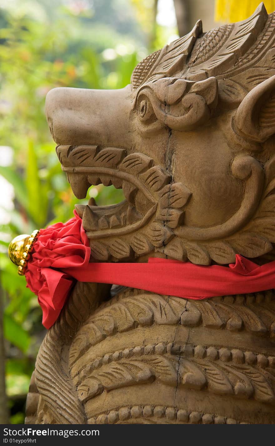 Carved wooden statue of a mythical demon guarding a door with a Chinese red bow around its neck. Carved wooden statue of a mythical demon guarding a door with a Chinese red bow around its neck