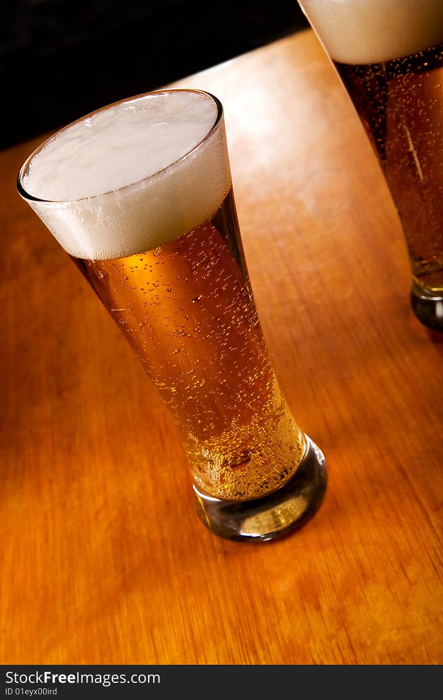 Two beer glasses on wood background, focus on first. Two beer glasses on wood background, focus on first