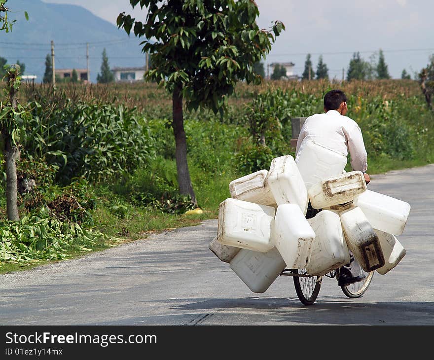 A man driving down the road with a bunch of barrels fastened to his bicycle. A man driving down the road with a bunch of barrels fastened to his bicycle