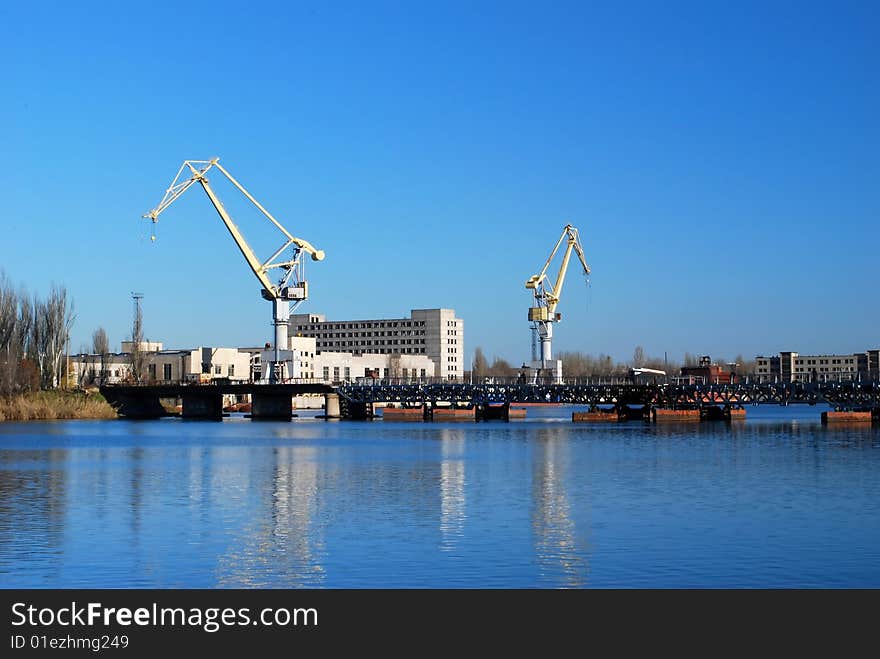 Two port cranes are reflected on the water surface. Metal bridge is crossing river. Two port cranes are reflected on the water surface. Metal bridge is crossing river.