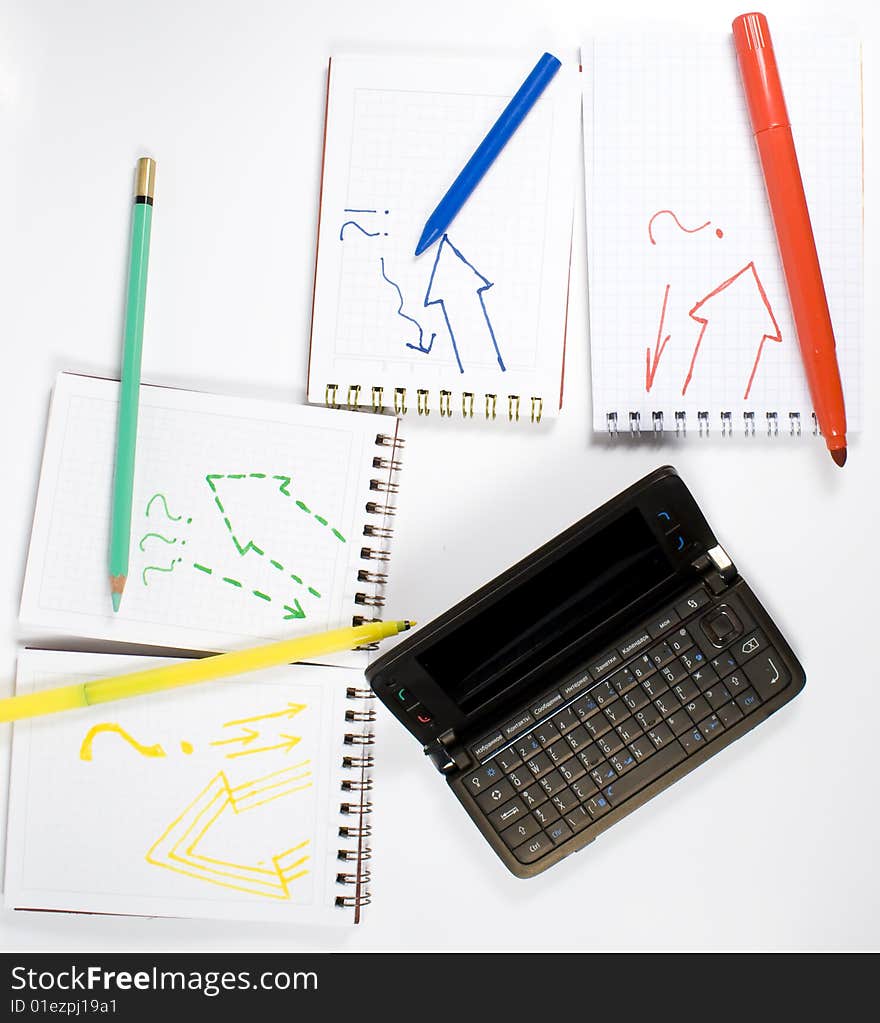 Open palmtop opposite four notebooks with felt-tip pens, crayon and wax pencil