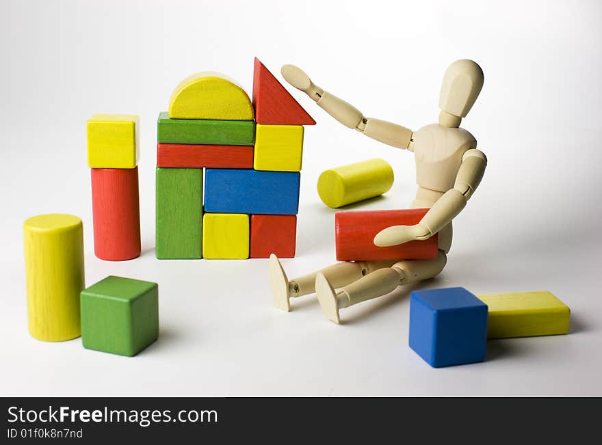 A wooden mannequin doll playing with colorful wooden toy blocks - cubes, building a house. A wooden mannequin doll playing with colorful wooden toy blocks - cubes, building a house.