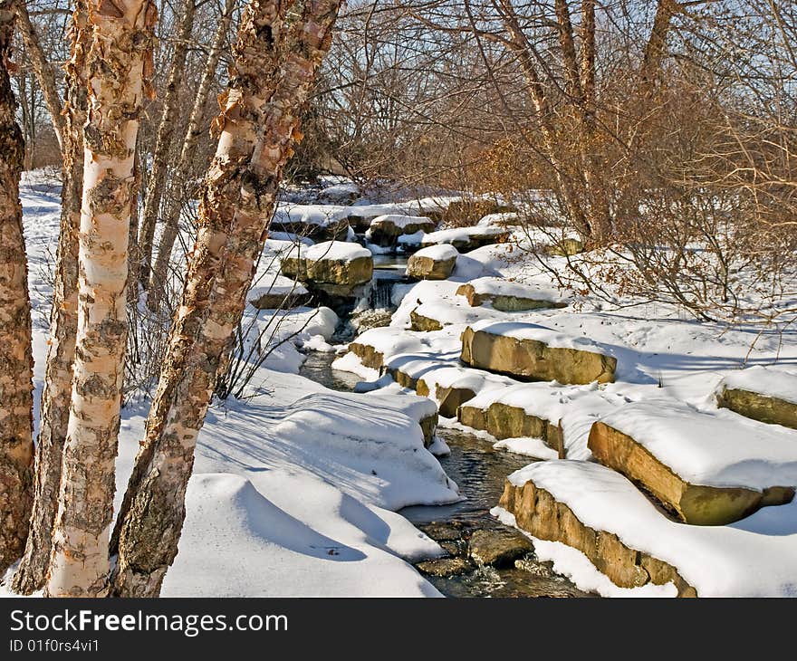 A snowy stream winding through trees and snow covered rocks