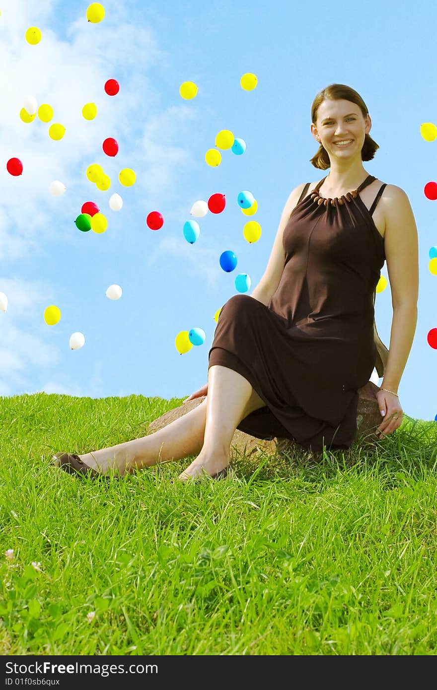 Smiling girl sitting on stone. Flying balloons on blue sky background.