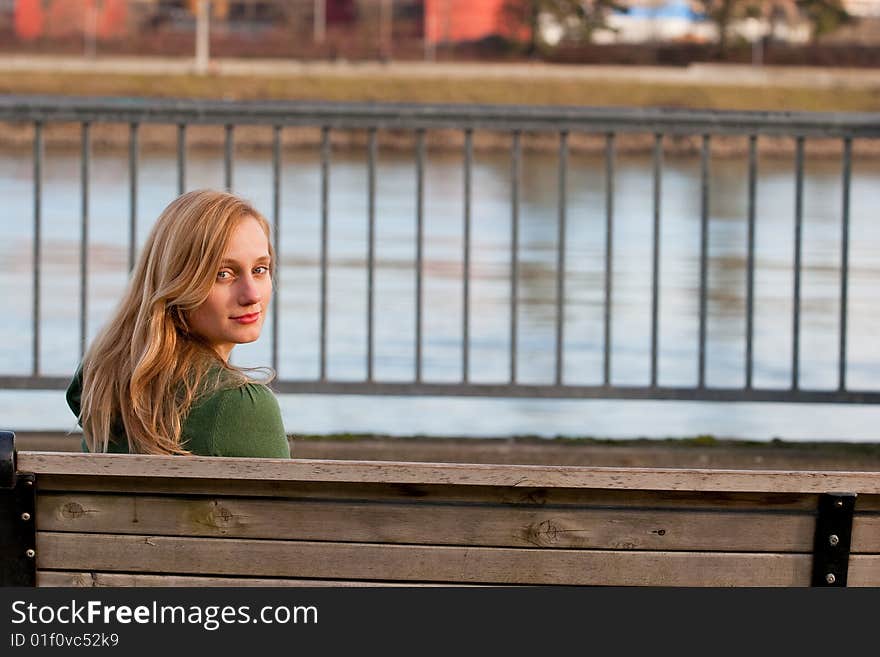 A female model sits on a bench by a river and looks back at the camera. A female model sits on a bench by a river and looks back at the camera.