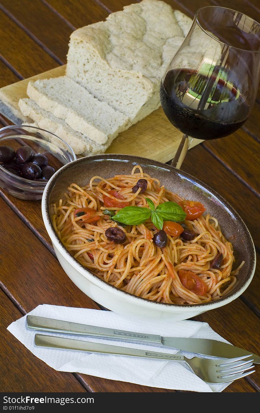 A plate of spaghetti with italian sauce, served with red wine, bread and olives on a wooden table