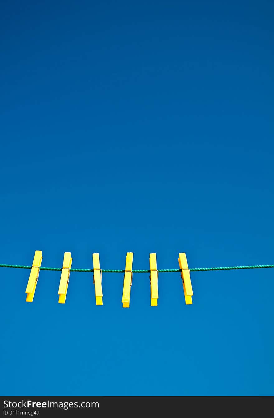 Yellow clothes pegs on a green washing line against a blue sky background.