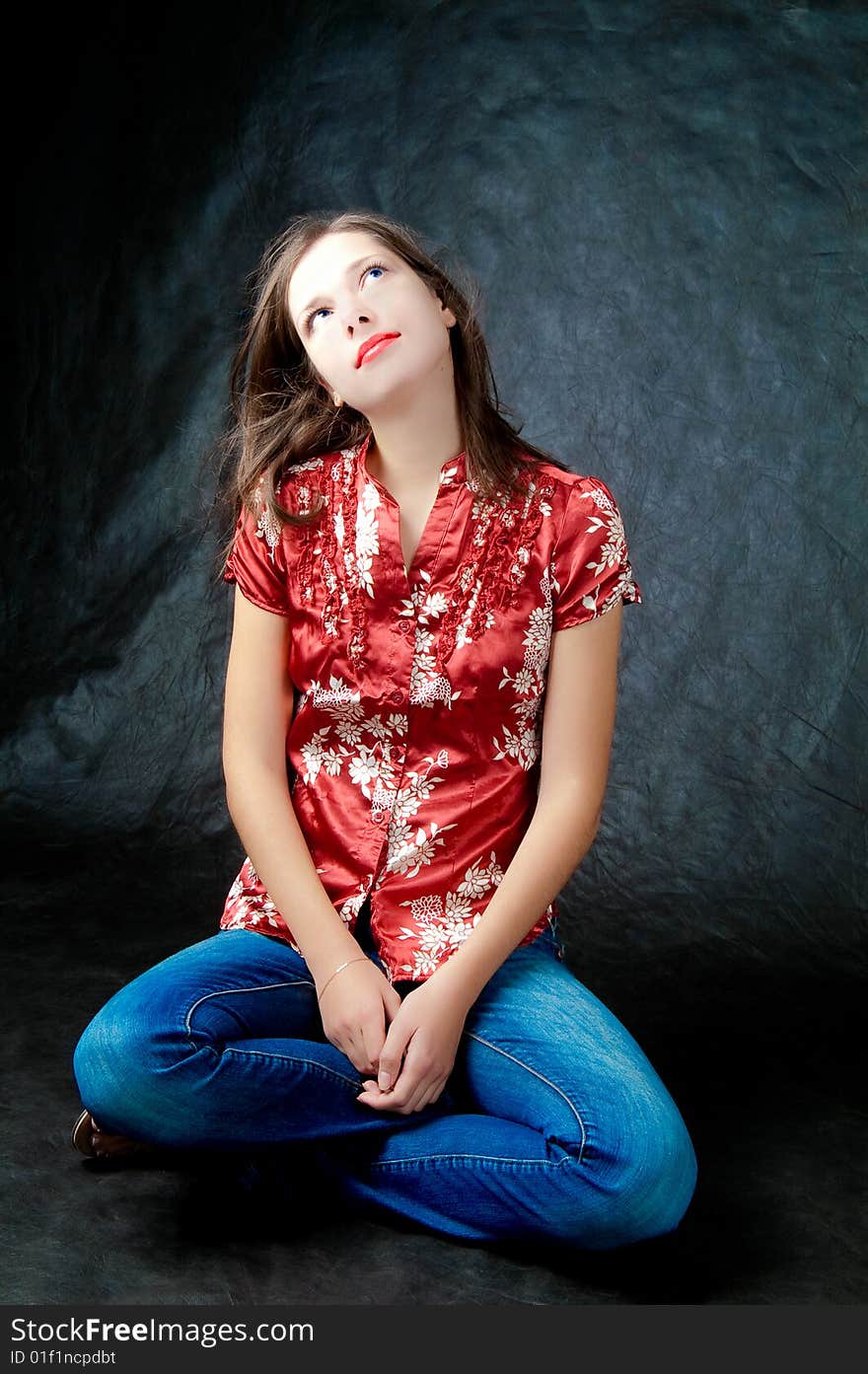 Young dark haired girl sitting with hands and legs crossed looking up thinking isolated on black background