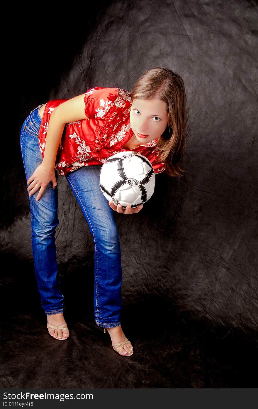 Young girl standing shaped with ball looking forward with hands supported hip isolated on black background