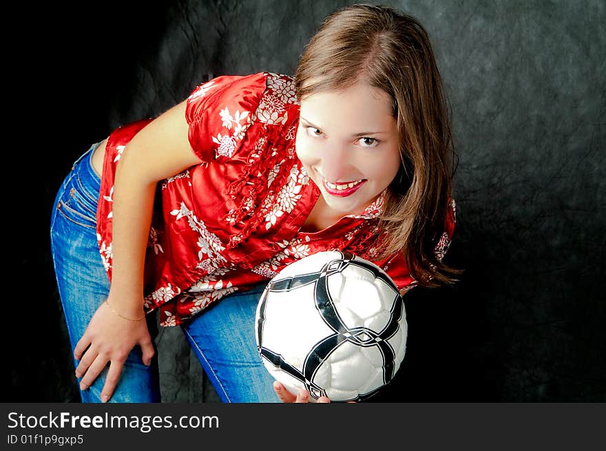 Young dark haired girl standing shaped with hand on hips holding ball and smiling on black background. Young dark haired girl standing shaped with hand on hips holding ball and smiling on black background