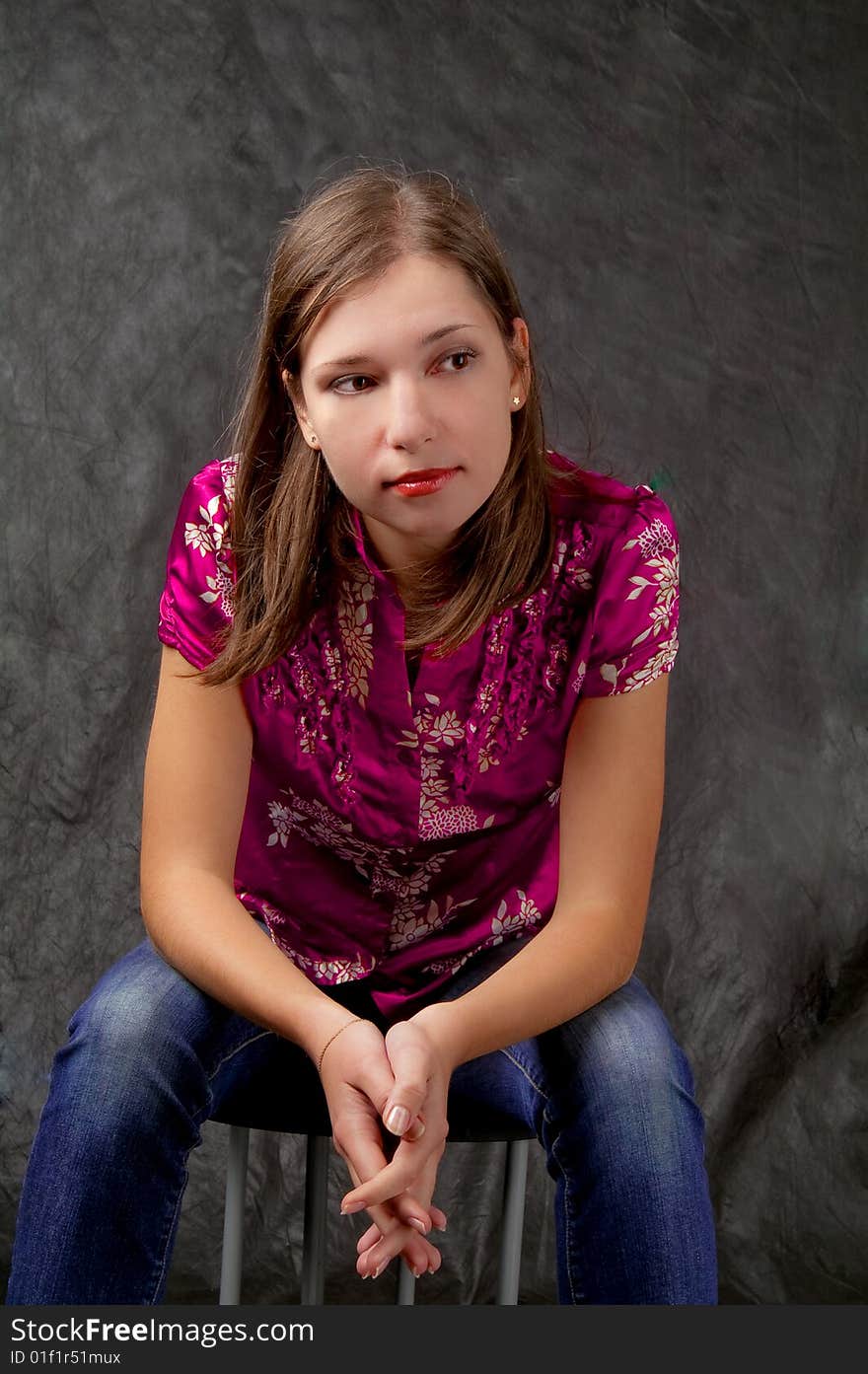 Young dark haired girl sitting on chair with hands crossed appear looking aside thinking isolated on black