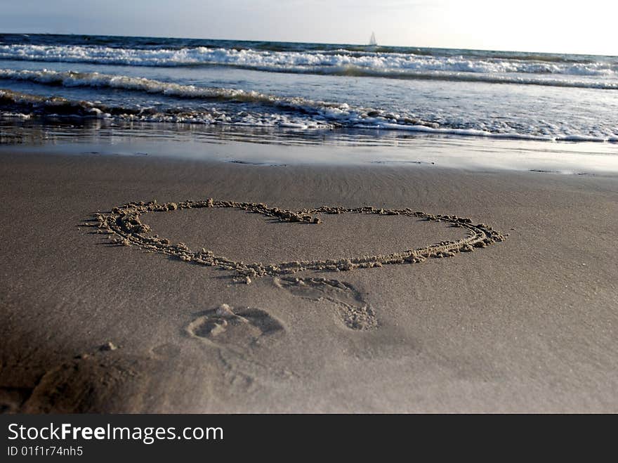 A heart drawn on sand and footprints of a girl, who left, but was watching a small boat to leave. A heart drawn on sand and footprints of a girl, who left, but was watching a small boat to leave