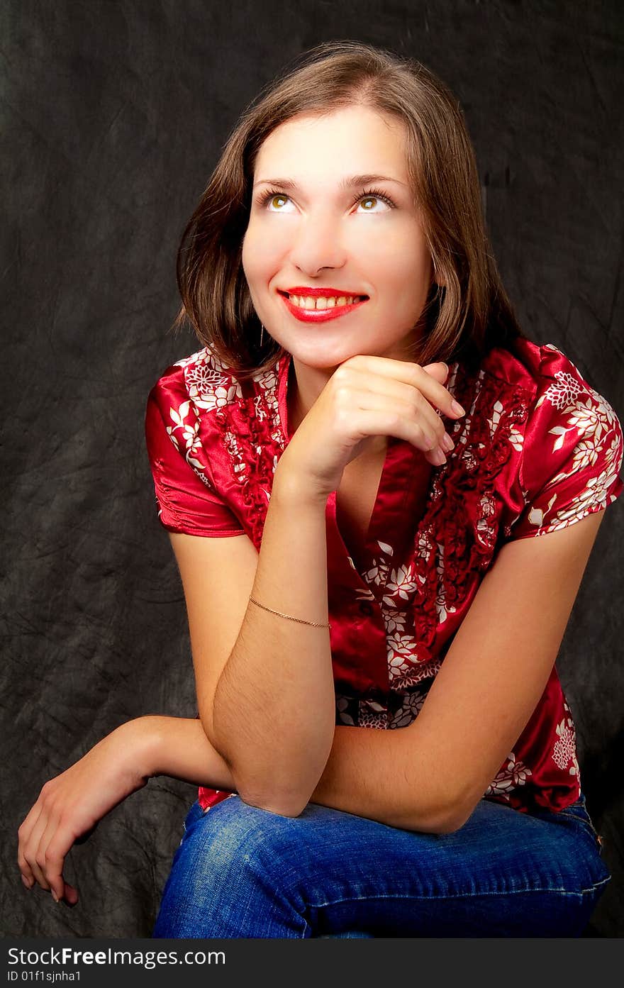 Pretty young dark haired girl sitting turned right side with hands crossed smiling looking up isolated on black. Pretty young dark haired girl sitting turned right side with hands crossed smiling looking up isolated on black