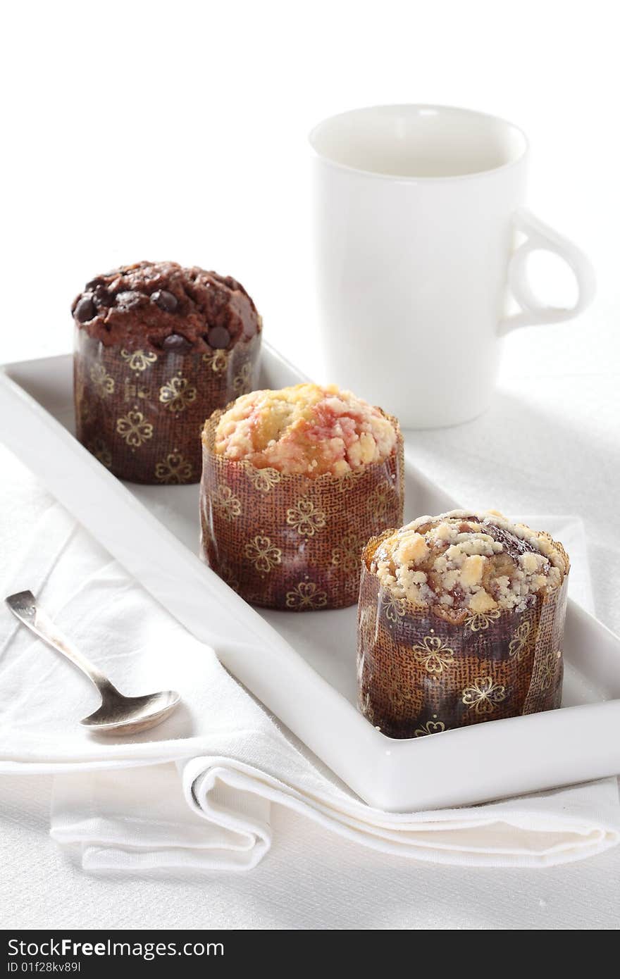 Three muffins, there are blueberry, cherry and chocolate muffin, with a white tea cup in background.