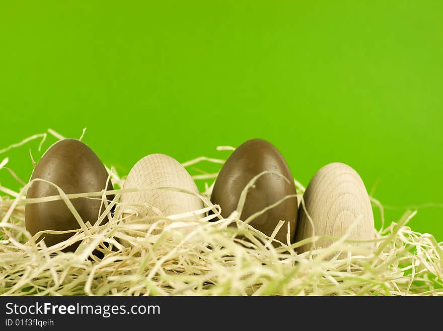 Chocolate and wooden easter eggs in a nest, arranged in a row, green background.