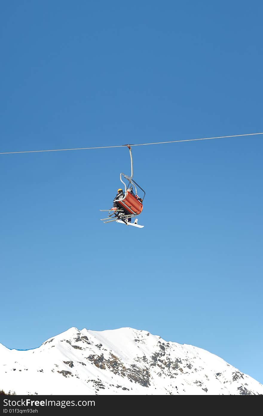 Skiers are riding in chairlift in a ski area, low angle view, Italy. Large copy-space at the top.