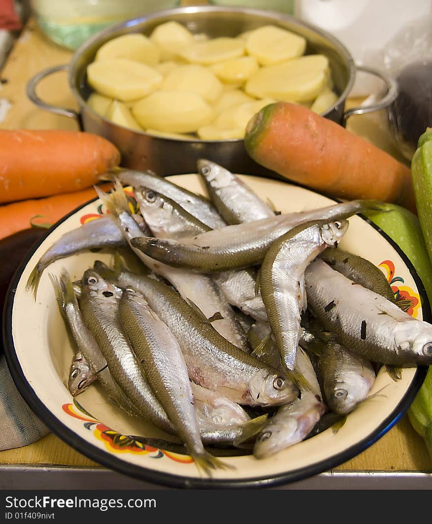 Many silver raw fish on yellow plate with orange carrot end green aubergine