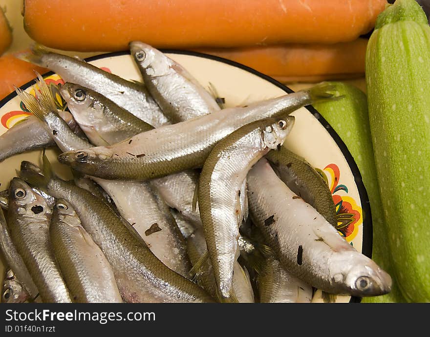 Many silver raw fish on yellow plate with orange carrot end green aubergine